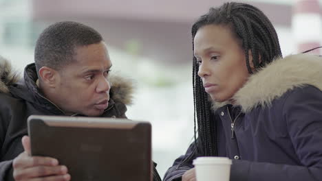 Afro-American-middle-aged-man-in-black-jacket-with-fur-hood-discussing-data-with-Afro-American-young-girl-with-braids