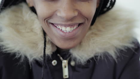 Close-up-shot-of-Afro-American-happy-young-girl-with-braids-in-grey-jacket-with-fur-hood--smiling-at-camera