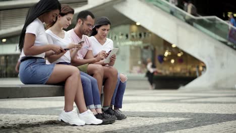 Calm-people-sitting-on-bench-with-modern-devices