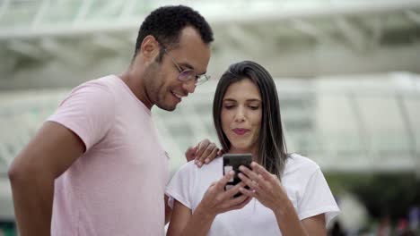 Smiling-good-friends-talking-while-looking-at-smartphone