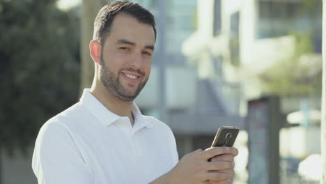 Smiling-bearded-man-with-smartphone-posing-during-sunny-day.