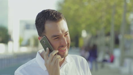 Emotional-smiling-young-man-talking-on-smartphone-outdoor.