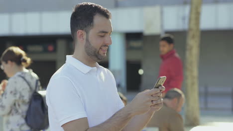 Side-view-of-smiling-bearded-man-texting-on-smartphone.