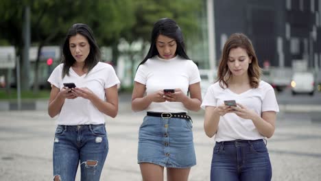 Peaceful-young-women-walking-on-street-with-smartphones