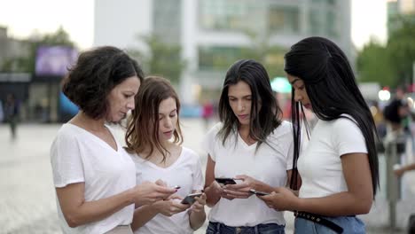 Concentrated-young-women-using-modern-phones-on-street