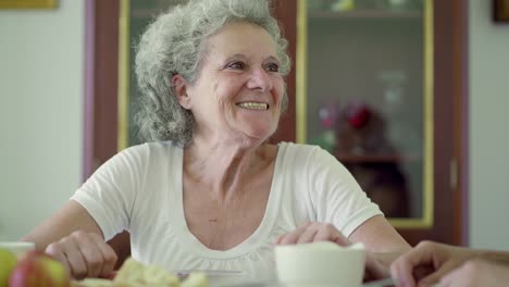 Cheerful-senior-woman-sitting-at-kitchen-table-and-talking.