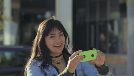 Smiling-young-woman-holding-green-smartphone-outdoor.