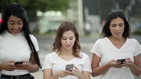 Cheerful-friends-walking-on-street-and-texting-on-phones
