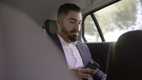 Focused-businessman-using-smartphone-and-laptop-in-car
