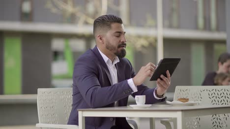 Serious-businessman-talking-and-using-tablet-pc-in-cafe