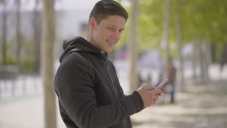 Young-man-using-smartphone-and-smiling-at-camera