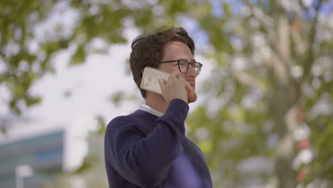 Bearded-man-in-eyeglasses-talking-by-smartphone-outdoor