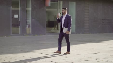 Businessman-with-laptop-drinking-from-paper-cup-outdoor