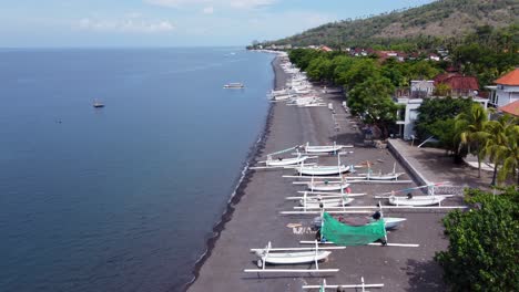 Barcos-De-Pesca-En-Canoa-Jukung-Blanca-Con-Estabilizadores-En-La-Playa-De-Arena-Negra-Volcánica-Del-Pueblo-De-Amed-En-Bali,-Indonesia