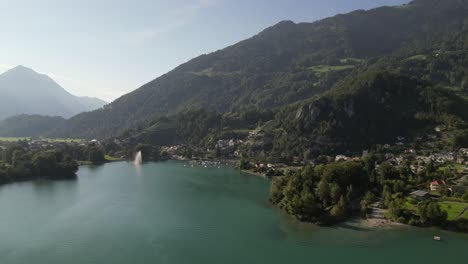 Aerial-shot-flying-over-a-blue-green-lake-towards-a-small-mountain-town-in-Switzerland
