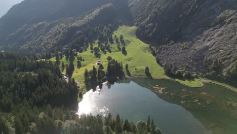 Vuele-Sobre-Un-Hermoso-Lago-En-Obersee-Nafels-En-Una-Deslumbrante-Región-Natural-Rodeada-De-Un-Bosque-De-Pinos-En-Una-Maravillosa-Puesta-De-Sol,-La-Superficie-Del-Agua-Refleja-El-Brillo-Del-Sol.
