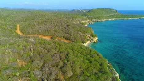Drone-side-to-side-dolly-rises-over-San-Juan-beach-Curacao,-overlooks-clear-ocean-water
