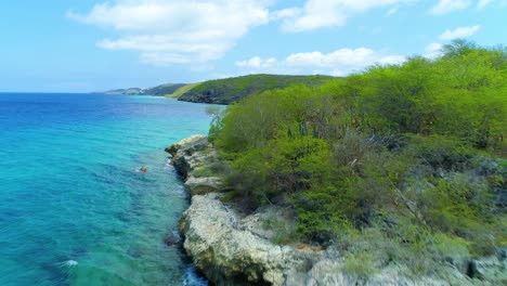 Drone-flies-over-bleached-white-rocky-cliff-and-shrubs-to-San-Juan-beach-Curacao