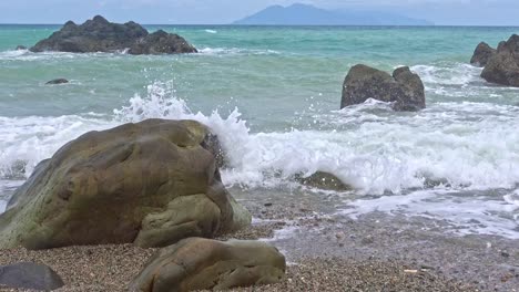 Low-angle-shot-of-waves-crashing-onto-rocks-along-the-coastline-of-Banbanon-Beach,-Surigao-Del-Norte,-Philippines-on-a-cloudy-day