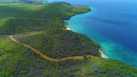 Tropical-dirt-road-leading-to-San-Juan-beach,-Curacao,-drone-high-angle-panoramic
