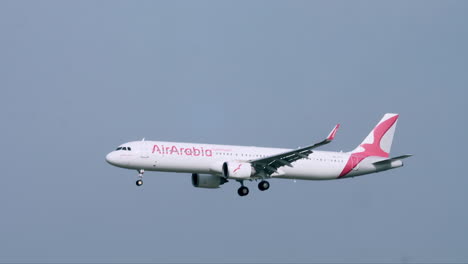 Air-Arabia-with-its-wheels-down-flying-towards-the-left-passing-by-an-Air-Traffic-Control-Tower-at-Suvarnabhumi-Airport-in-Bangkok