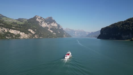 Drohnenansicht-Eines-Weißen-Schiffes,-Das-über-Blaues-Wasser-Am-Fuße-Einer-Wunderschönen-Bergkette-Fährt