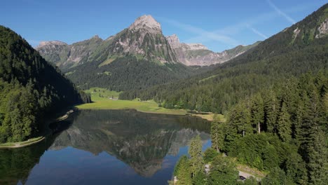 Drone-shot-mountain-reflection-in-calm-lake-water-surrounded-by-pine-tree-forest-in-Switzerland-obersee-nafels-highland-in-summer-sunny-day-blue-sky-and-scenic-wonderful-green-background-travel-swim