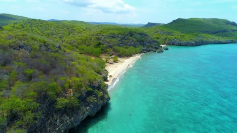 Drone-rises-along-rocky-jagged-cliff-with-San-Juan-golden-sandy-beach-and-turquoise-water