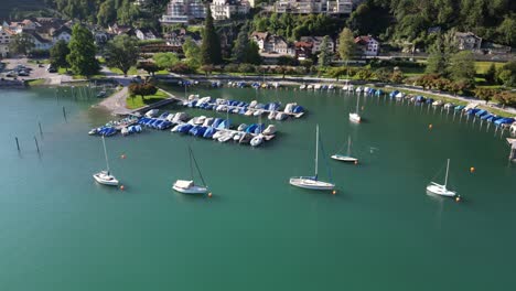 Aerial-view-of-blue-and-white-boats-docked-on-beautiful-blue-green-waters-near-a-lakeside-town
