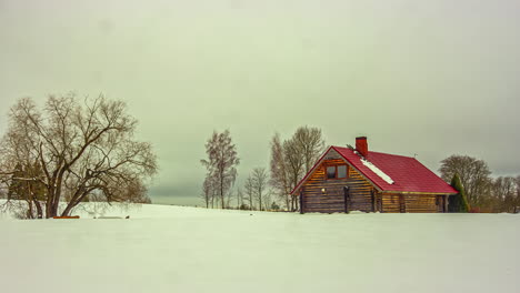 Cinematic-timelapse-shot-of-the-sunset-behind-clouds-in-a-snowy-landscape-with-a-house-with-red-roof-in-focus