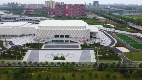 Aerial-panning-establishment-shot-of-the-beautiful-Weihai-Olympic-Center-in-Shandong,-China-overlooking-a-soccer-field-and-the-city-in-classical-Chinese-architecture-in-the-morning