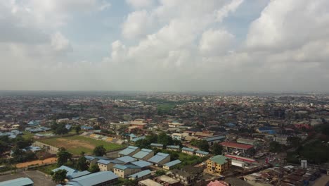 Vista-Aérea-De-La-Comunidad-En-Lagos-Nigeria-En-Un-Día-Nublado-Con-Drones-Cayendo-Para-Revelar-Una-Carretera-Con-Autos-Y-Camiones-Moviéndose-Rápidamente