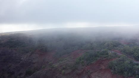 Low-descending-aerial-shot-flying-through-thick-clouds-towards-a-mountain-road-near-Waimea-Canyon-in-Kaua'i,-Hawai'i