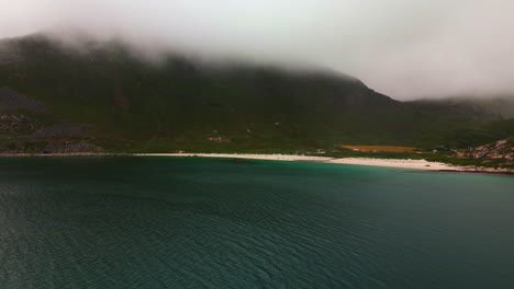 Cinematic-aerial-shot-of-the-famous-Haukland-beach-in-the-lofoten-islands-in-the-arctic-north-on-a-cloudy-and-foggy-summer-day-with-green-water,-Drone