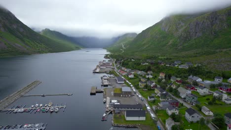 Aerial-dolly-forward-shot-of-the-small-town-of-Gryllefjord-nestled-in-the-valley-of-cloud-draped-mountains-on-a-magical-summer-day