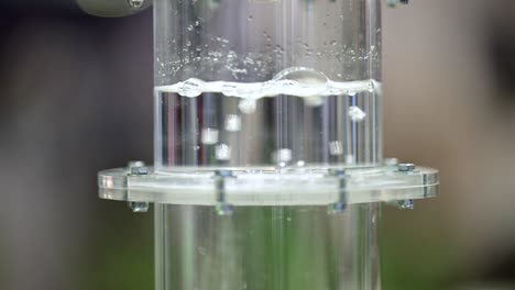 Hydrogen-gas-is-bubbeling-through-a-membrane-in-a-plastic-cylinder-filled-with-water,-close-up