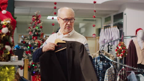Older-man-examining-elegant-blazers-in-busy-bustling-shopping-store-during-winter-holiday-season.-Elderly-customer-in-Christmas-decorated-store-checking-clothing-size,-looking-for-perfect-fit