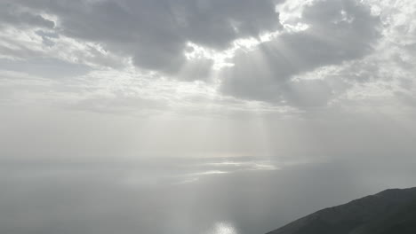 Drone-shot-from-the-Llogara-view-point-near-Tirana-in-Albania-on-a-cloudy-day-in-the-shadows-looking-over-the-sea-with-god-rays-shining-through-the-clouds-onto-the-sea-water-LOG