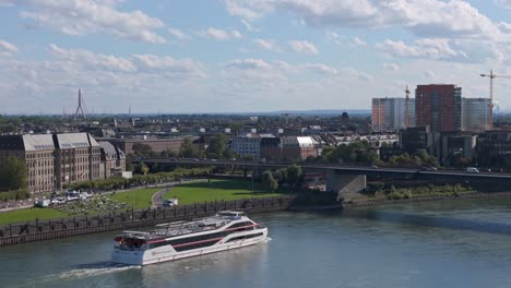 KD-Passenger-ferry-sailning-under-Rheinkniebrücke-bridge,-aerial-drone-cityscape-of-Düsseldorf,-Germany