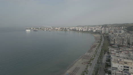 Disparo-De-Drone-Sobre-La-Ciudad-Vlore-Albania-Mirando-Hacia-Los-Edificios-Y-El-Puerto-Con-Ferry-Con-El-Mar-Y-La-Playa-Debajo-En-Un-Día-Soleado-Con-Un-Poco-De-Neblina