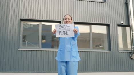 Female-Protester-Holding-a-Message-"Save-the-Planet"-in-Front-of-a-Laboratory-Building-Wearing-Blue-Protective-Outfit