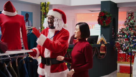 Manager-wearing-Santa-Claus-costume-around-shopping-mall-fashion-boutique-to-spread-holiday-joy.-Supervisor-in-festive-themed-suit-showing-cheerful-client-red-garment-piece