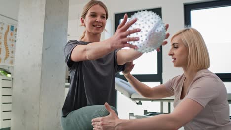 Female-physical-therapist-working-with-young-woman-using-exercising-ball.