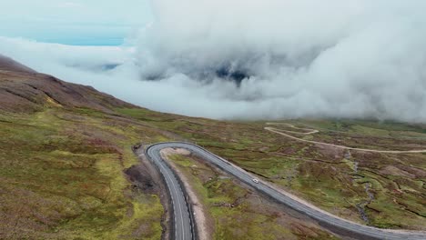 Vuele-Sobre-La-Carretera-Asfaltada-En-Las-Laderas-De-Las-Montañas-Con-Un-Paisaje-Nublado-Al-Fondo-En-El-Este-De-Islandia
