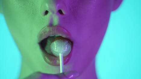 Close-up-of-a-woman's-lips-while-she-sexy-licks-a-delicious-lollipop-with-her-tongue-and-encloses-it-with-her-lips-for-a-sweet-moment-against-turquoise-background-with-green-purple-contrast-in-face