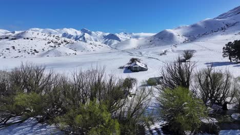 Remote-shed-in-farm-and-drone-over-tree-line-reveal-amazing-winter-mountains-scenery,-New-Zealand