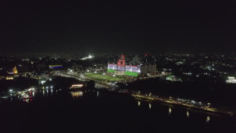 During-the-nighttime-lake-reflection-road-with-vehicles,-drone-footage-heading-in-the-direction-of-the-Telangana-State-New-Secretariat,-which-is-decorated-with-lights,-was-recorded-in-4K