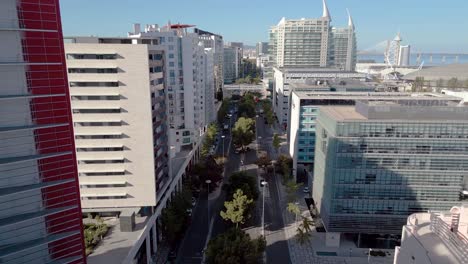 Urban-Avenue-with-Modern-Buildings-in-an-Office-Area-in-Lisbon,-Vasco-da-gama-Bridge-in-the-Background,-Traveling-Back-Shot