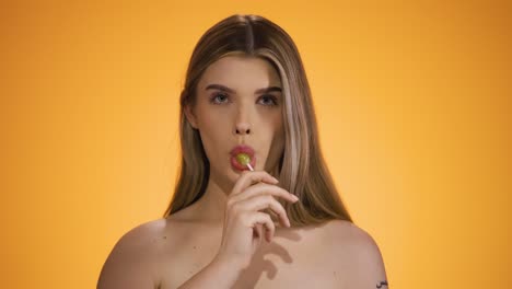 Static-medium-shot-of-a-Seductive-Blonde-Young-Caucasian-Woman-Licks-a-delicious-sweet-Lollipop-and-enjoy-the-candy-against-Chroma-Background-Staring-with-Naked-Torso