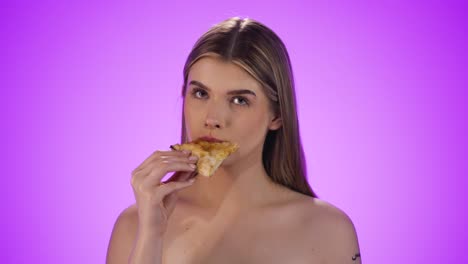 Static-medium-shot-of-a-young-model-taking-a-bite-of-a-delicious-and-tasty-pizza-to-fight-her-hunger-in-front-of-purple-background-in-slow-motion